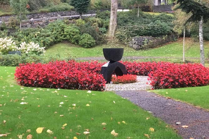 Minnestein omgitt av blomster i anonym minnelund på Arendal kirkegård.