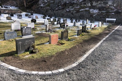 Nylagt kantstein langs grusvei på Hisøy kirkegård, som tydelig markerer overgangen mellom vei og plen. Flere gravsteiner står på rekke, og det er nylig jordlagt og sådd til langs kantsteinen. Noe snø ligger fortsatt i bakgrunnen, men solen skinner og markerer overgangen til vår. Foto.