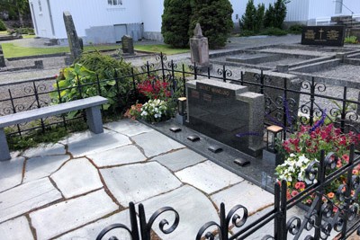 Navnet minnelund på Hisøy kirkegård med navneplater, blomster og benk innenfor smijernsgjerde.